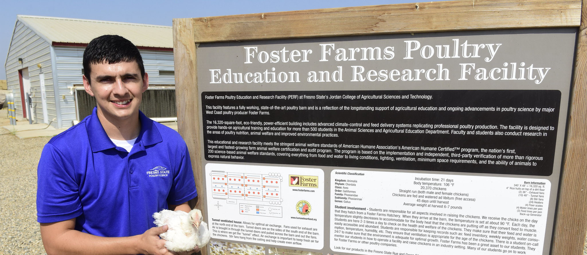 Rodrigo Lopez holding chicken in front of Foster Farms Education and Research Facility sign