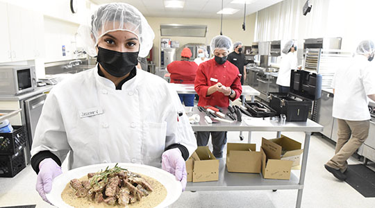 Student preparing steak dish in culinology lab