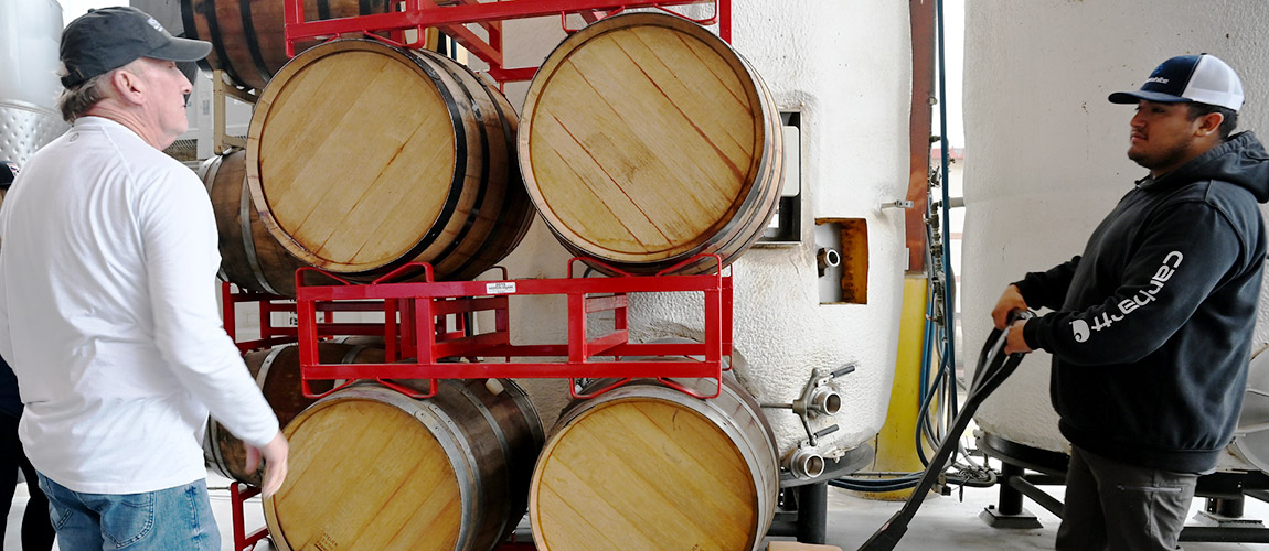 Tom Montgomery and Alberto Ramirez move barrels at campus winery.