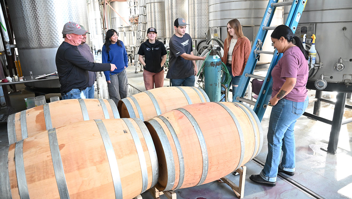 Winemaker and students process wines next to tanks and barrels at campus winery.
